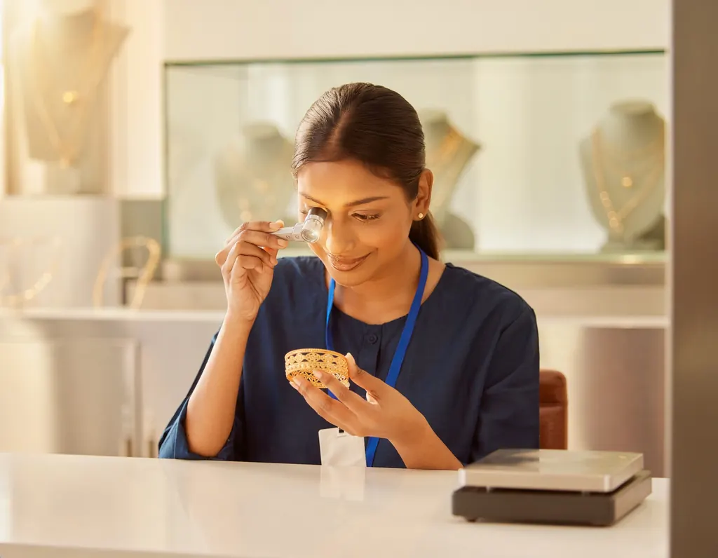 A gold appraiser examining a gold bangle through a jeweller’s loupe at a jewellery counter